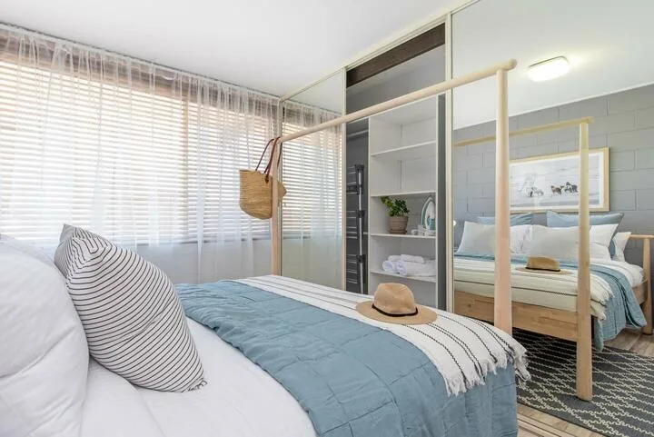 Un dormitorio luminoso con una cama bien arreglada y un armario con espejo.
