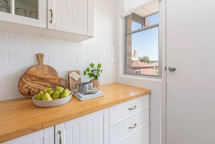 Una luminosa encimera de cocina está bajo armarios blancos junto a una ventana.