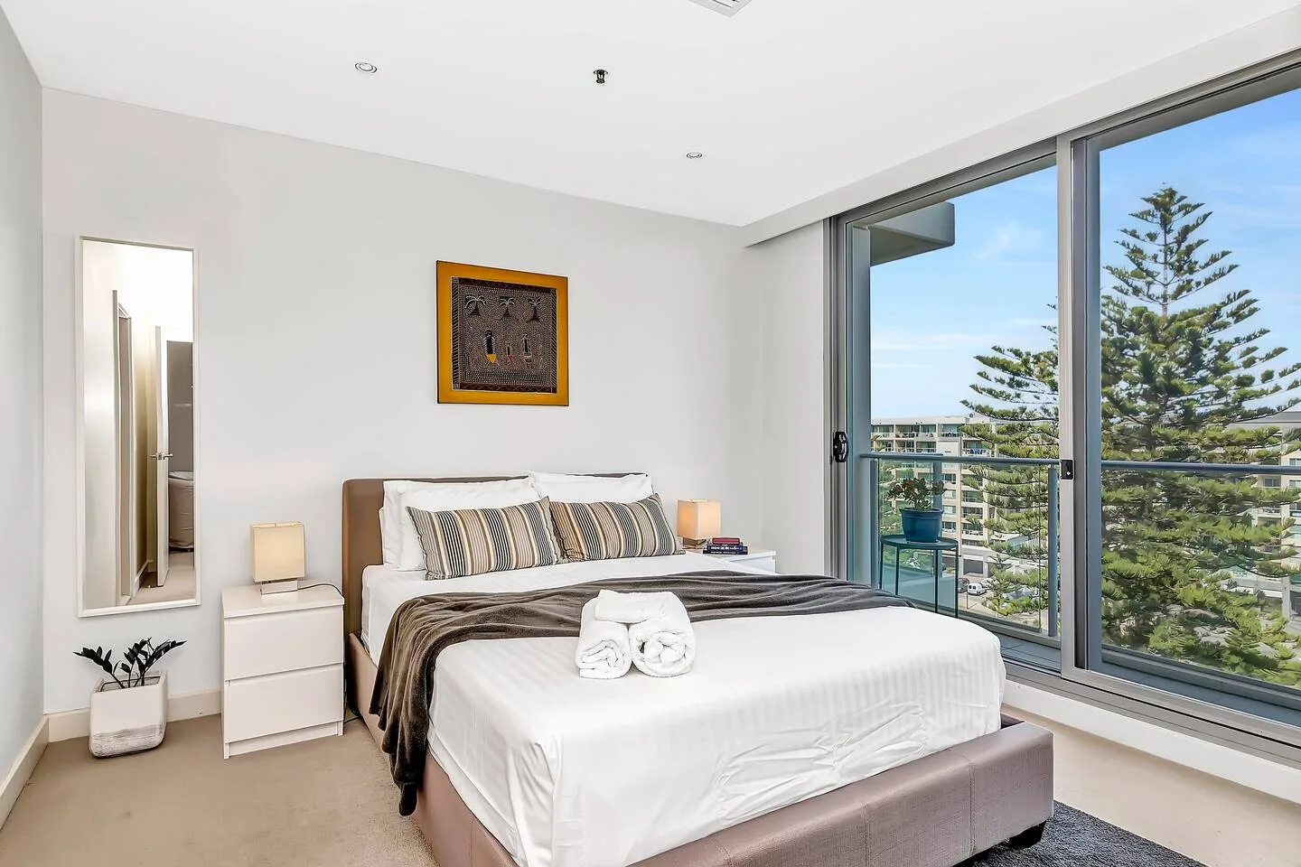 Un dormitorio luminoso con una cama tendida junto a grandes ventanales con vistas a la vegetación.