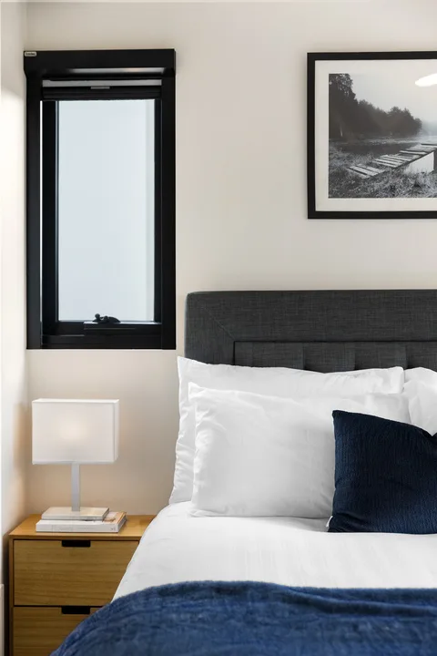 Un dormitorio con una cama bien hecha, un cabecero oscuro y un cuadro enmarcado.