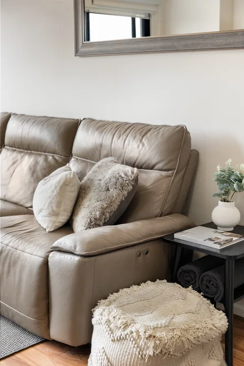 Una sala de estar con un sofá de cuero, cojines decorativos y una mesita auxiliar.