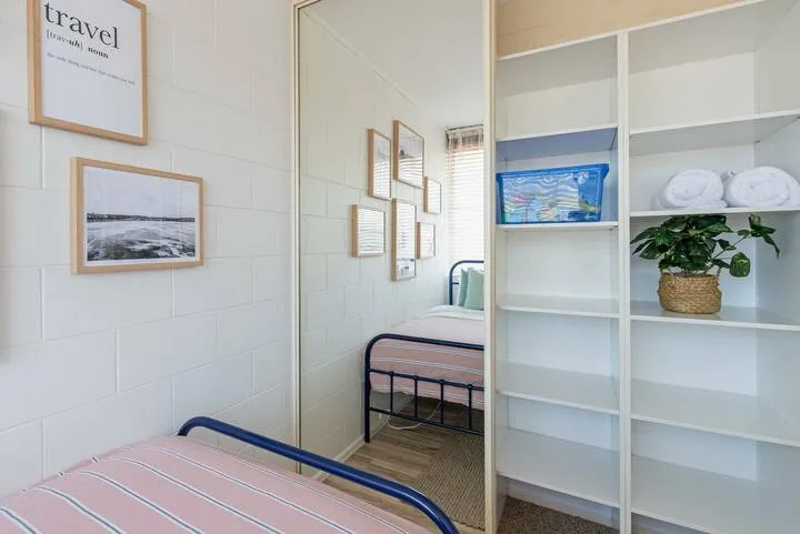 Un dormitorio luminoso con una cama de metal, estanterías empotradas y cuadros en la pared.