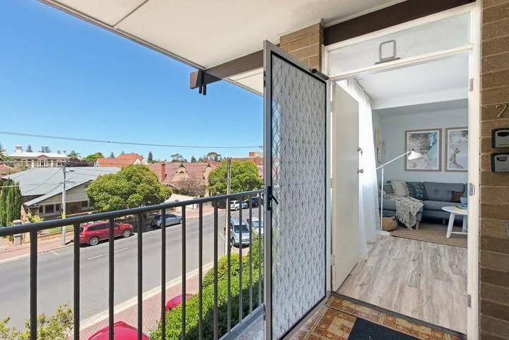 Un balcón abierto da a una calle, con una sala visible a través de la puerta.