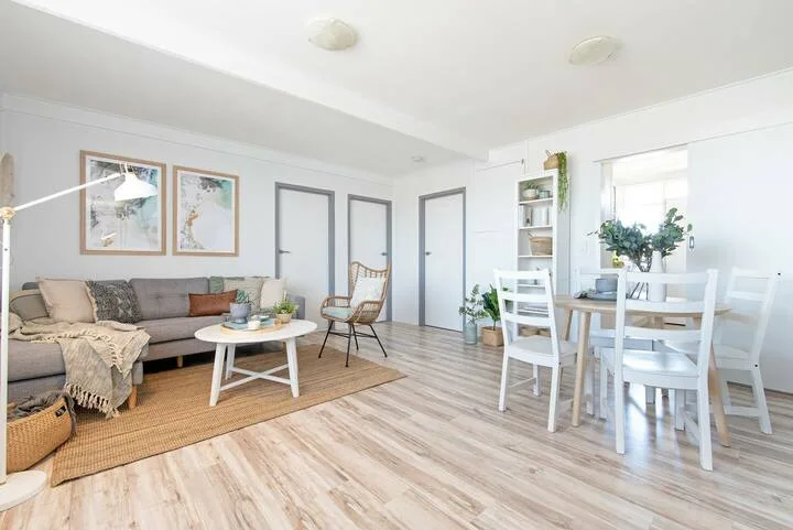 Una luminosa sala de estar y comedor con asientos, una mesa y ventanas grandes.