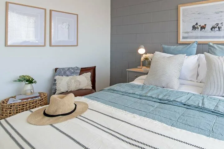 Dormitorio con una cama vestida con ropa de cama azul y cuadros en las paredes.