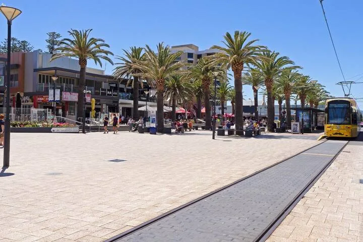 Una plaza al aire libre con palmeras y un tranvía sobre las vías.