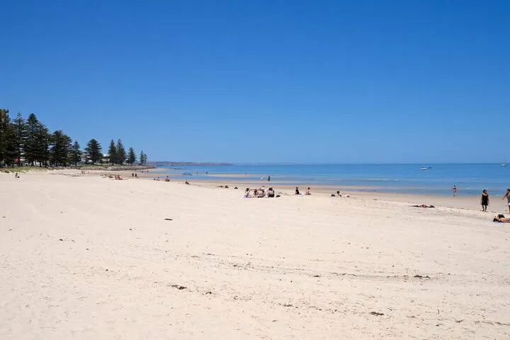 Una playa de arena se extiende junto al agua tranquila bajo un cielo despejado.