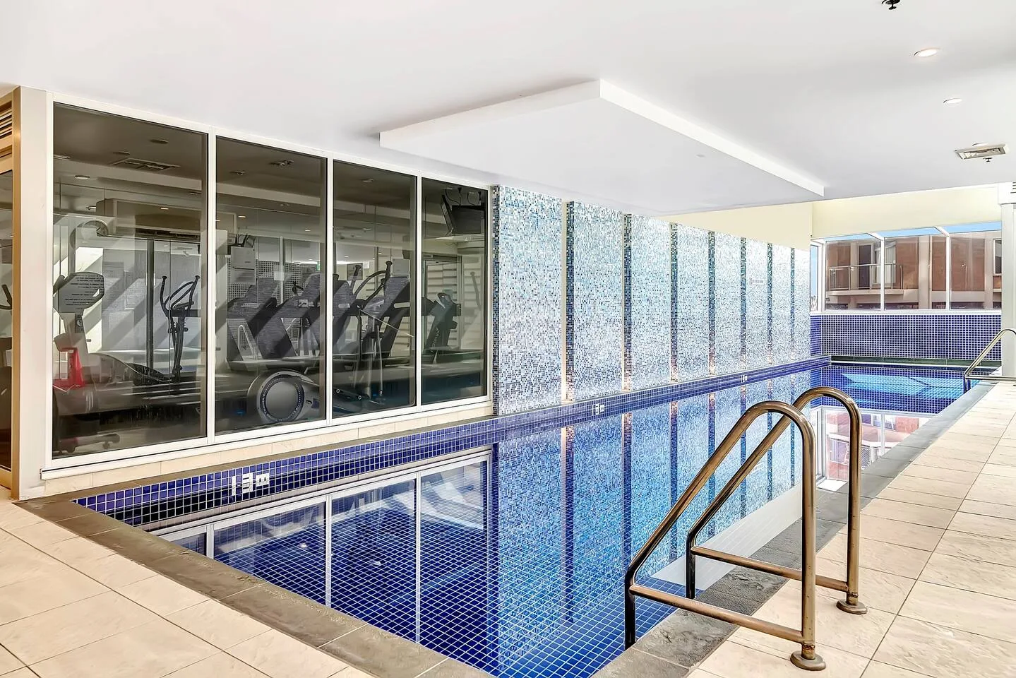 Una piscina cubierta junto a una zona de ejercicio con paredes de vidrio.