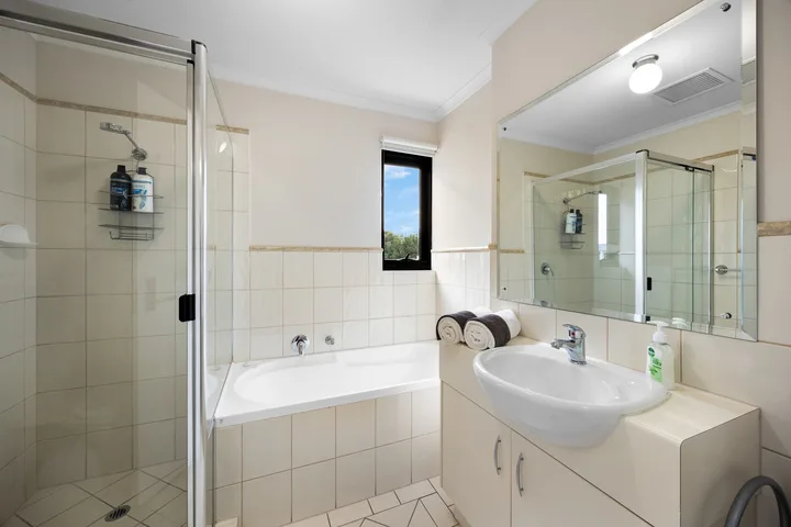 Un baño alicatado con bañera, ducha de vidrio y lavabo con mueble.