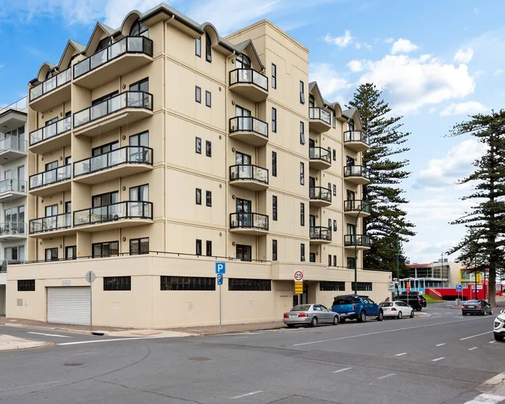 Un edificio de apartamentos de varios pisos con balcones está junto a una calle.