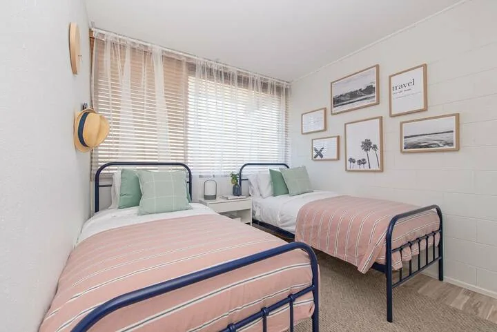 Un dormitorio con dos camas, ropa de cama rosa claro y una ventana luminosa.