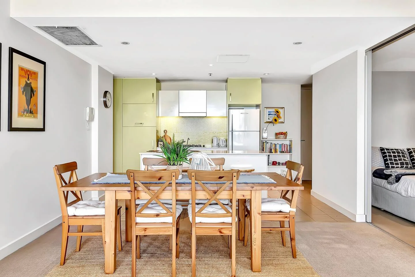 Un comedor con mesa y sillas de madera da a una cocina abierta.