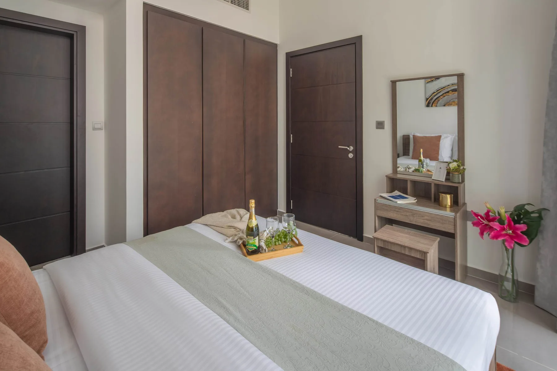 Un dormitorio con una cama bien tendida, puertas oscuras y un espejo sobre una cómoda.