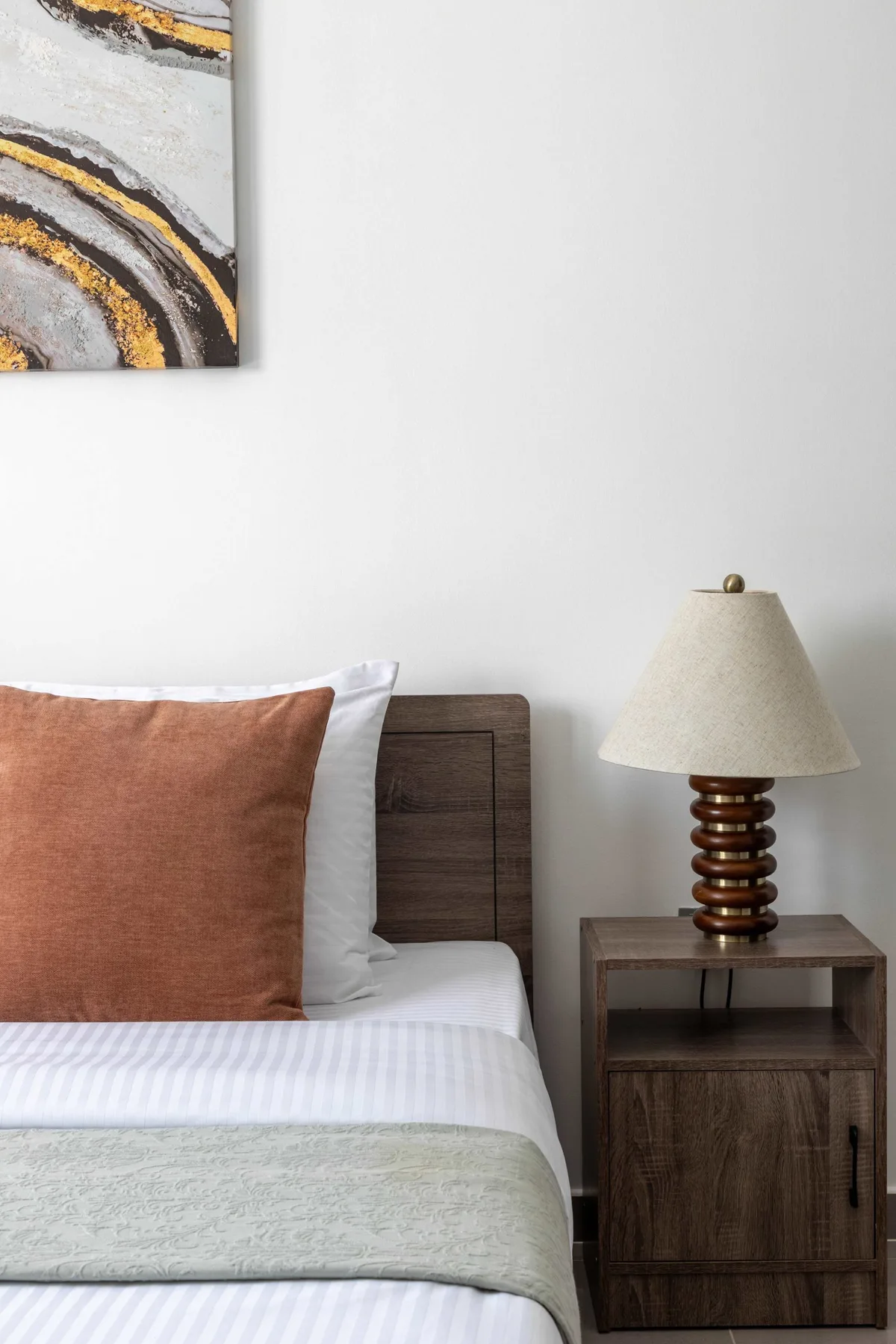Un dormitorio con una cama bien tendida, una mesita de noche y una lámpara.