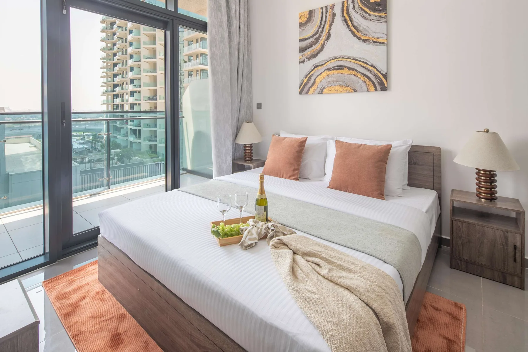 Dormitorio con una cama tendida junto a grandes puertas de vidrio que dan a un balcón.