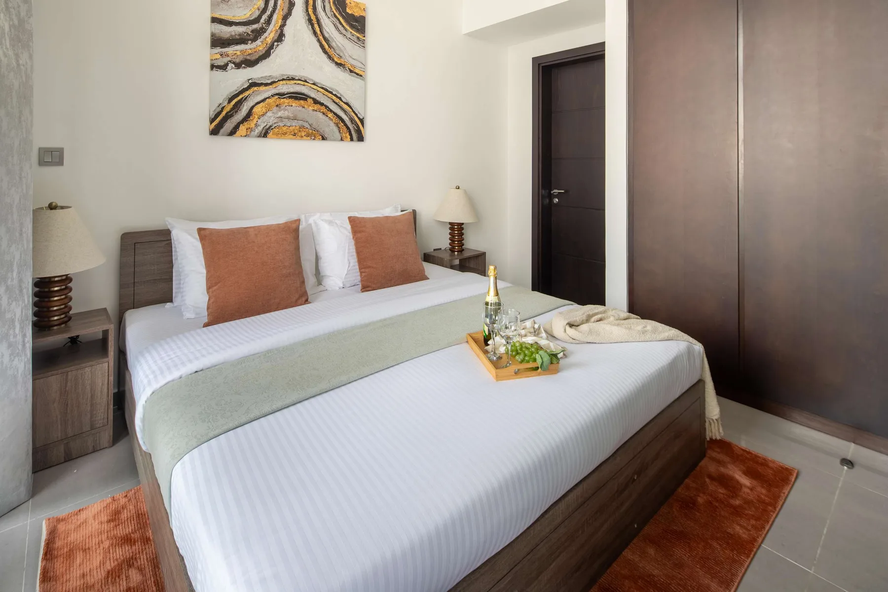 Un dormitorio con una cama tendida, cojines color óxido y arte abstracto en la pared.