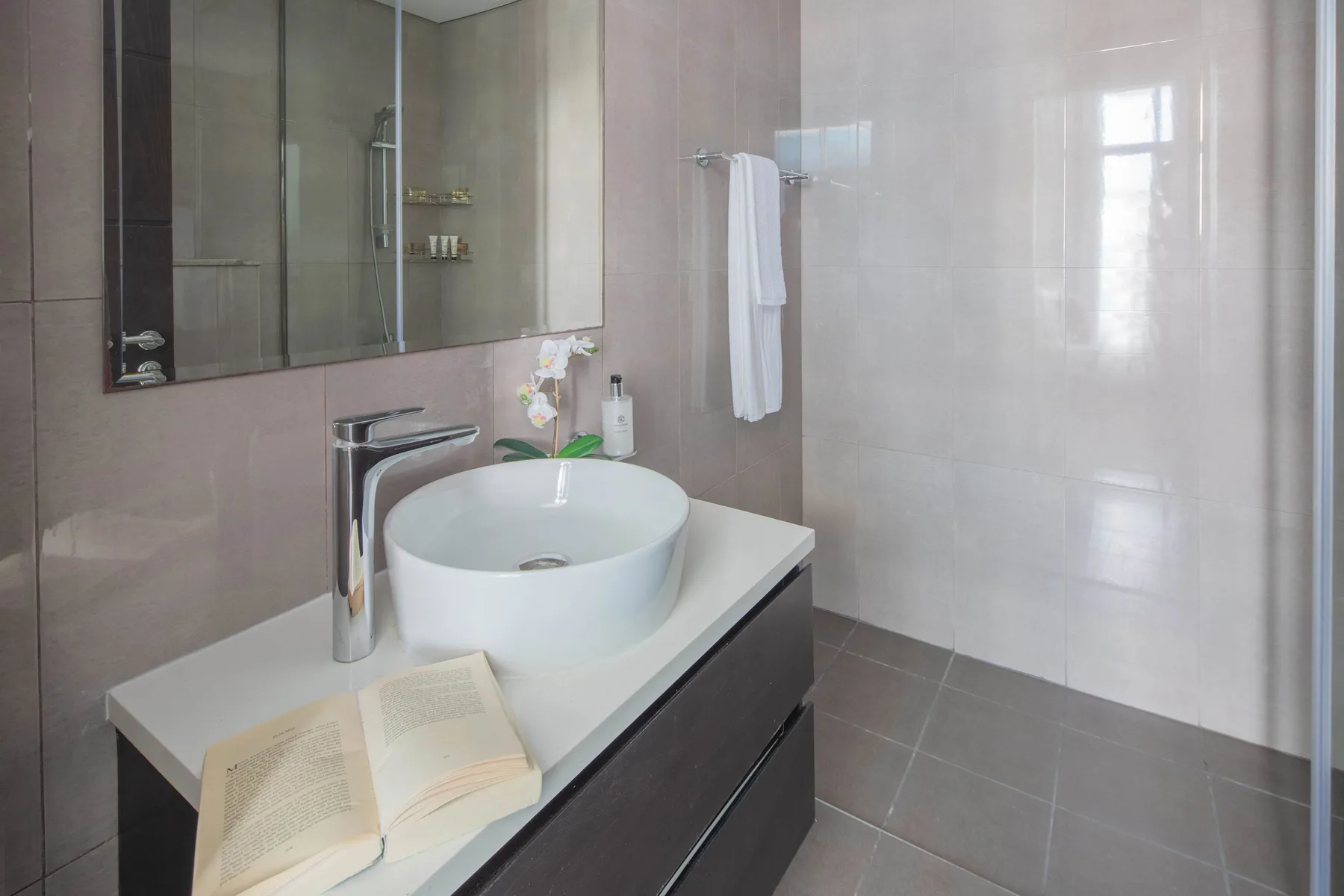 Baño moderno con lavabo sobre encimera, espejo y zona de ducha alicatada.