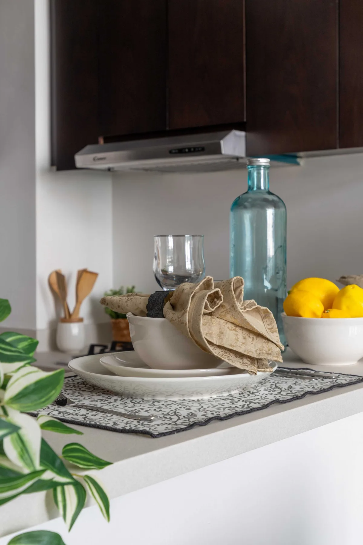 Una encimera de cocina con platos, una botella azul de vidrio y un cuenco de limones.