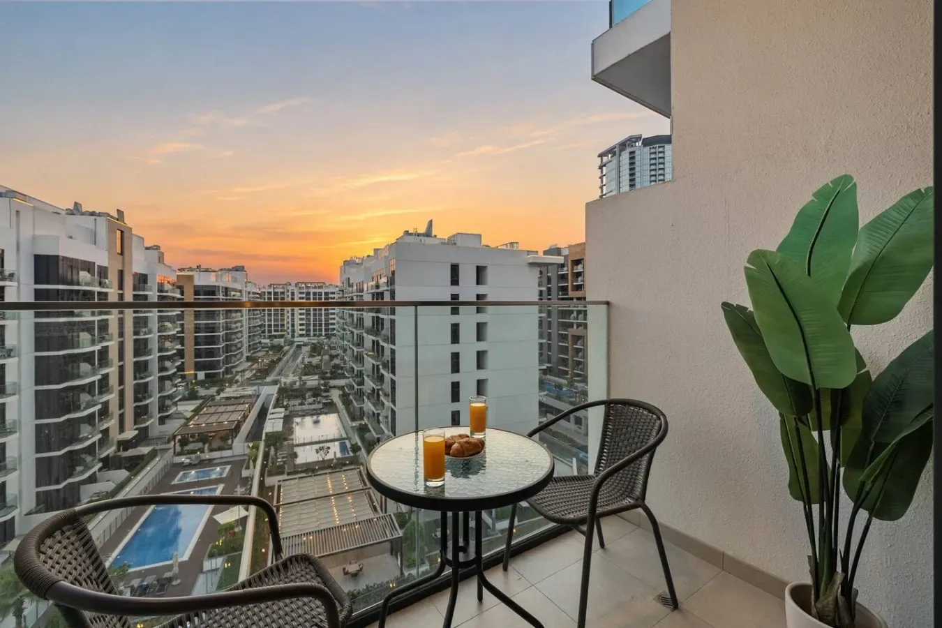 A balcony seating area overlooks nearby buildings beneath a colorful sunset sky.