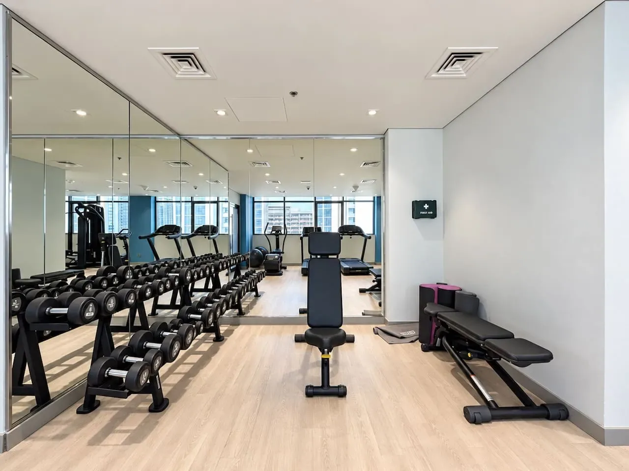 A fitness room with weight racks, exercise benches, and mirrored walls.