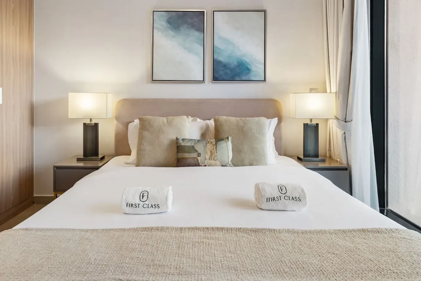 A neatly made bedroom features a bed beneath two framed abstract paintings.