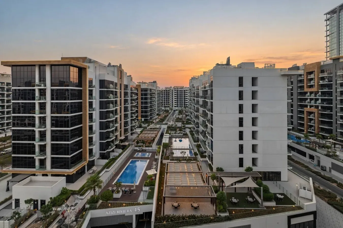 A modern apartment complex surrounds landscaped courtyards and swimming pools at sunset.