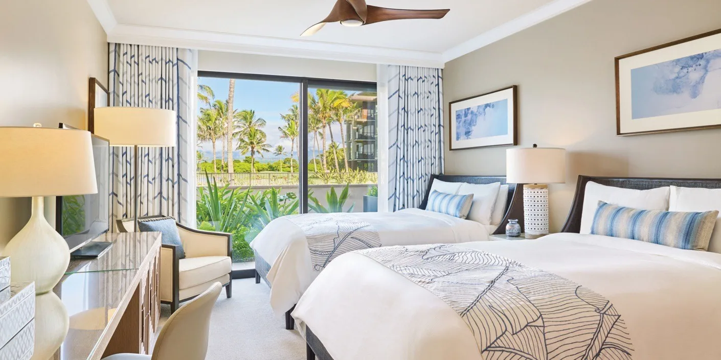 A bright bedroom with two beds facing a large window overlooking palm trees.