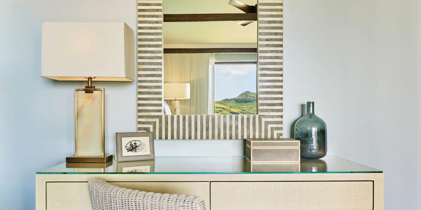 Una cómoda de dormitorio con espejo de marco rayado, lámpara y objetos decorativos.