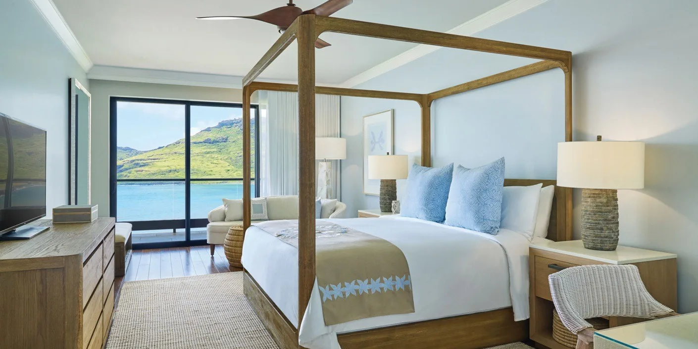 A bright bedroom with a canopy bed, bedside tables, and a lake view through the windows.