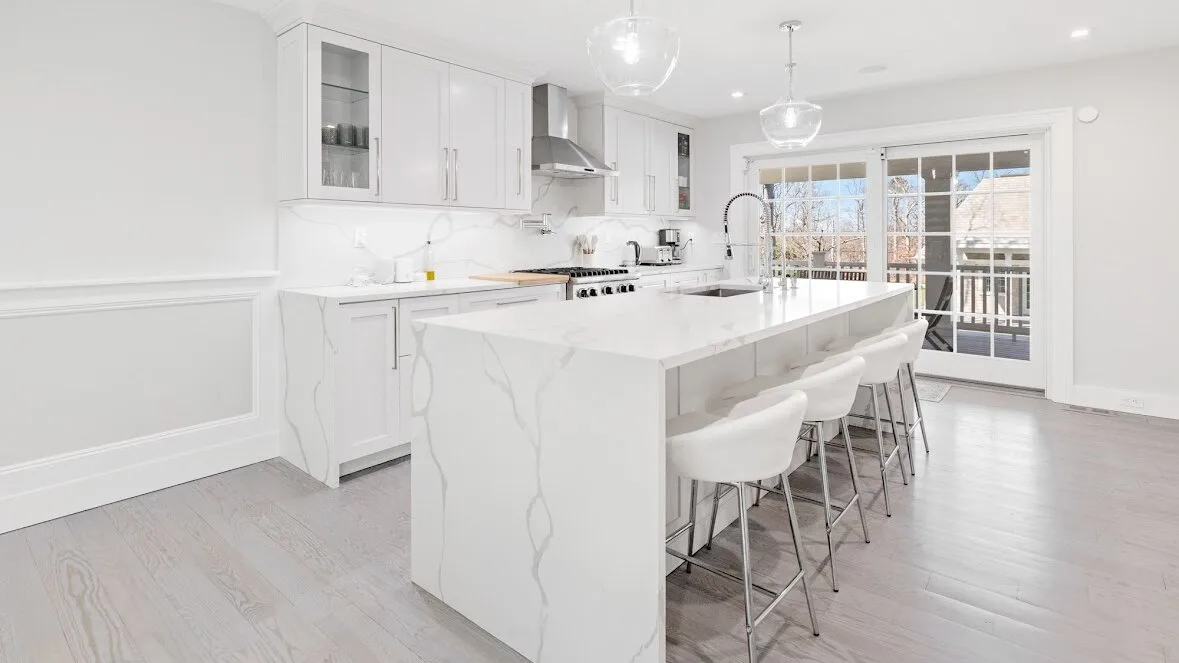 Una cocina moderna y luminosa con una gran isla y asientos junto a puertas de vidrio.
