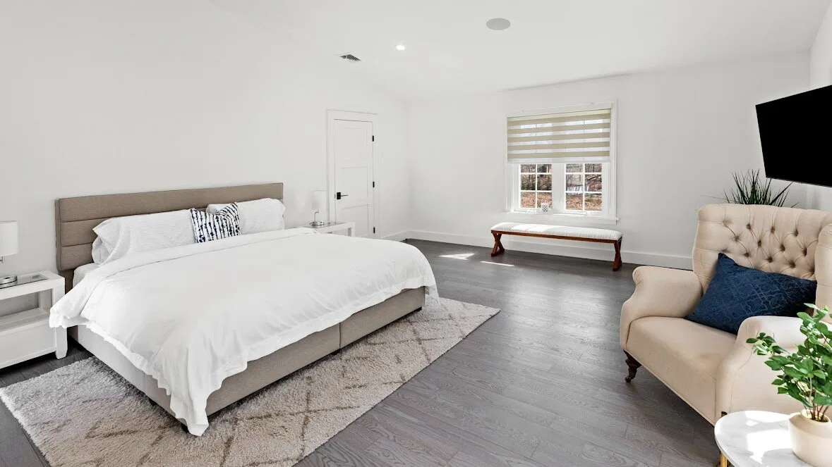 Un dormitorio luminoso con una cama, una ventana y un sillón tapizado.