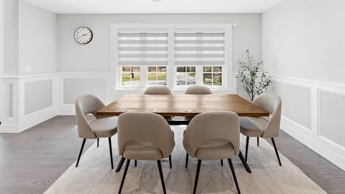 Un comedor luminoso con una mesa de madera, asientos tapizados y ventanas amplias.