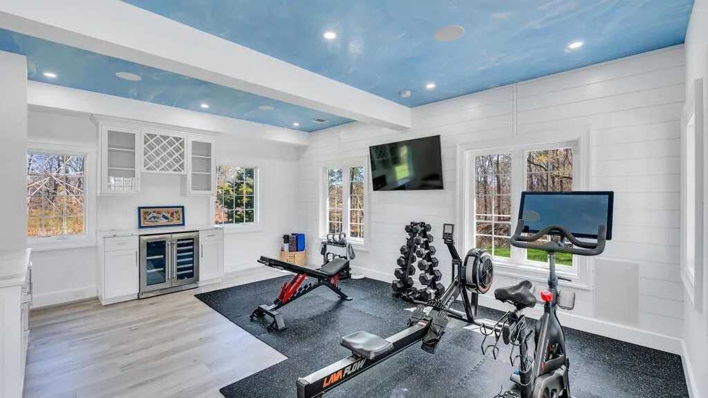 Un gimnasio luminoso con equipos de ejercicio y ventanas grandes.