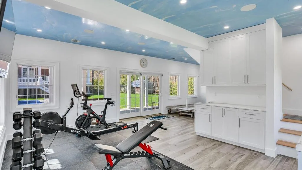 Un gimnasio luminoso con equipo de ejercicio y ventanas grandes.