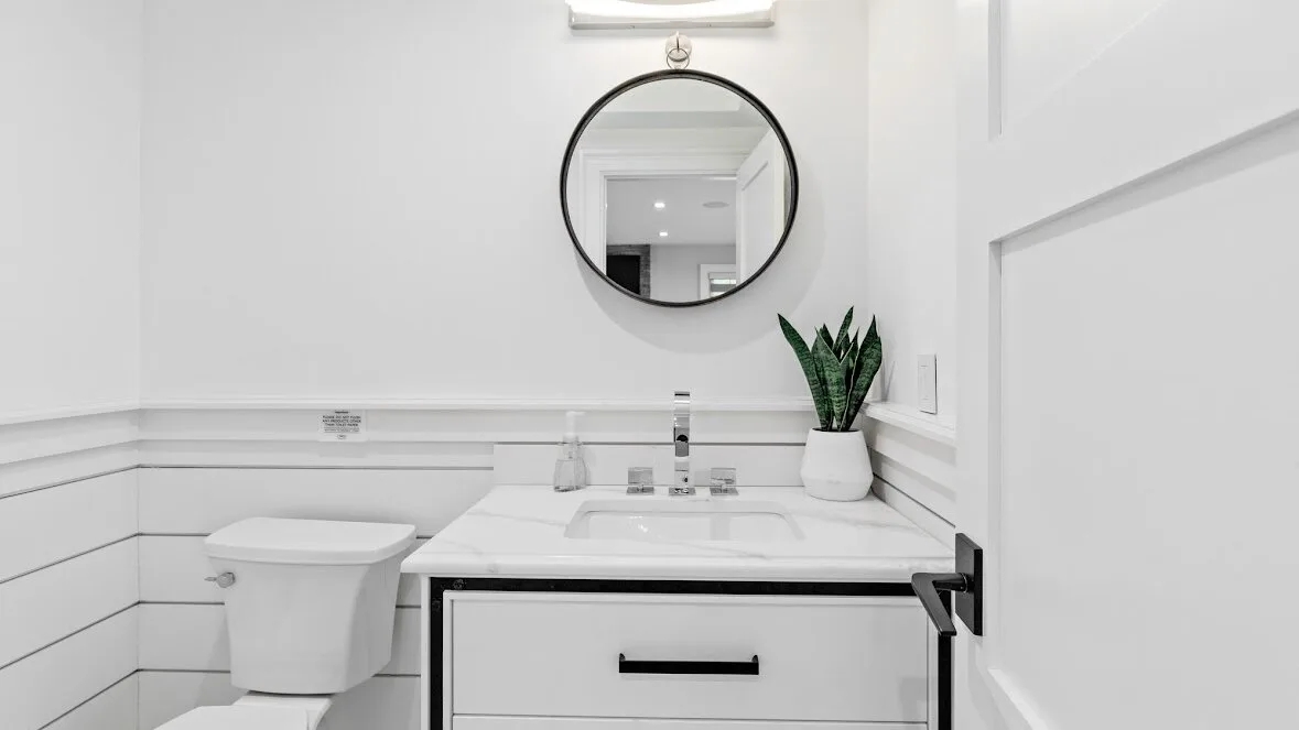 Un baño luminoso con lavabo, espejo redondo e inodoro.