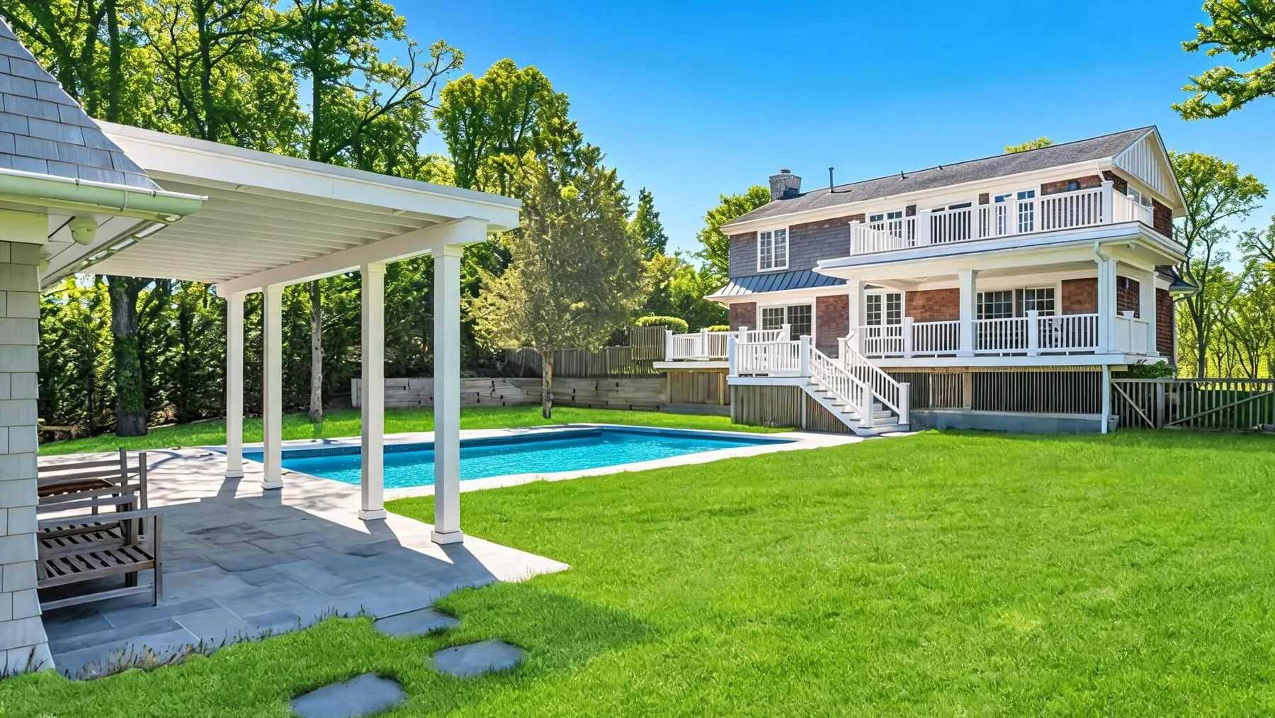 Un patio trasero con piscina, césped verde y un patio cubierto.