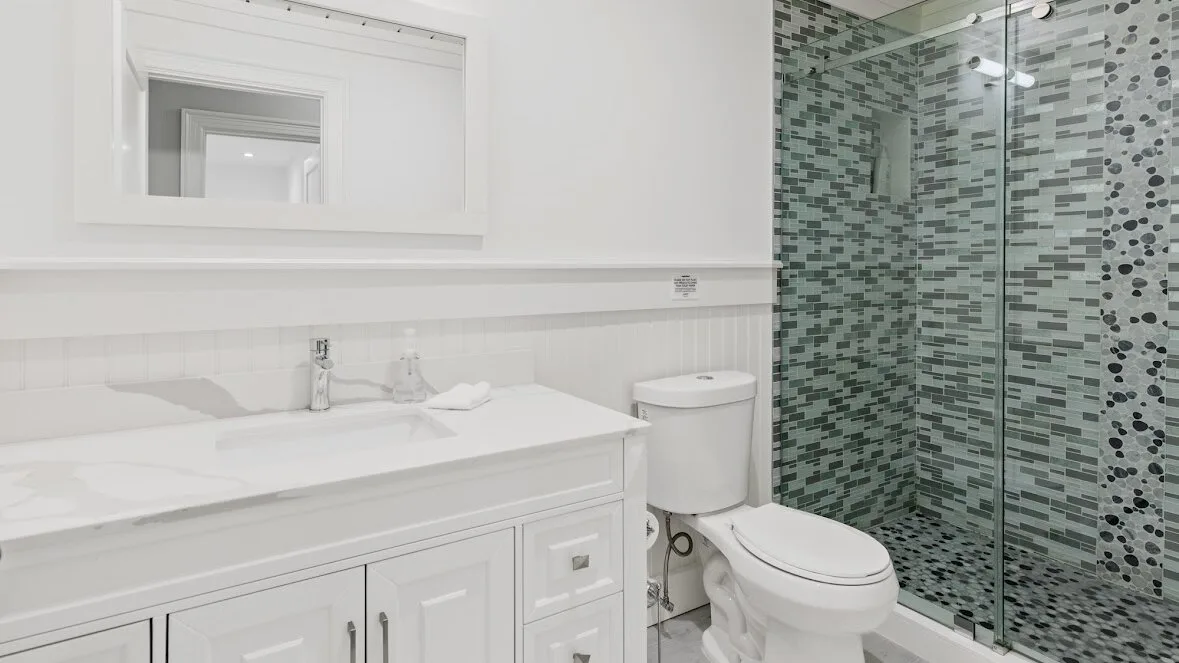 Un baño luminoso con tocador blanco, inodoro y ducha con cerramiento de vidrio.