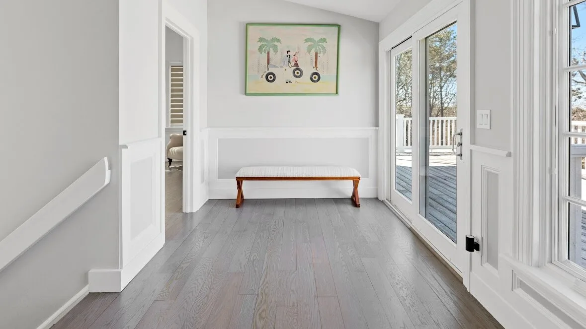 Una entrada luminosa con suelo gris, un banco de madera y puertas de vidrio.