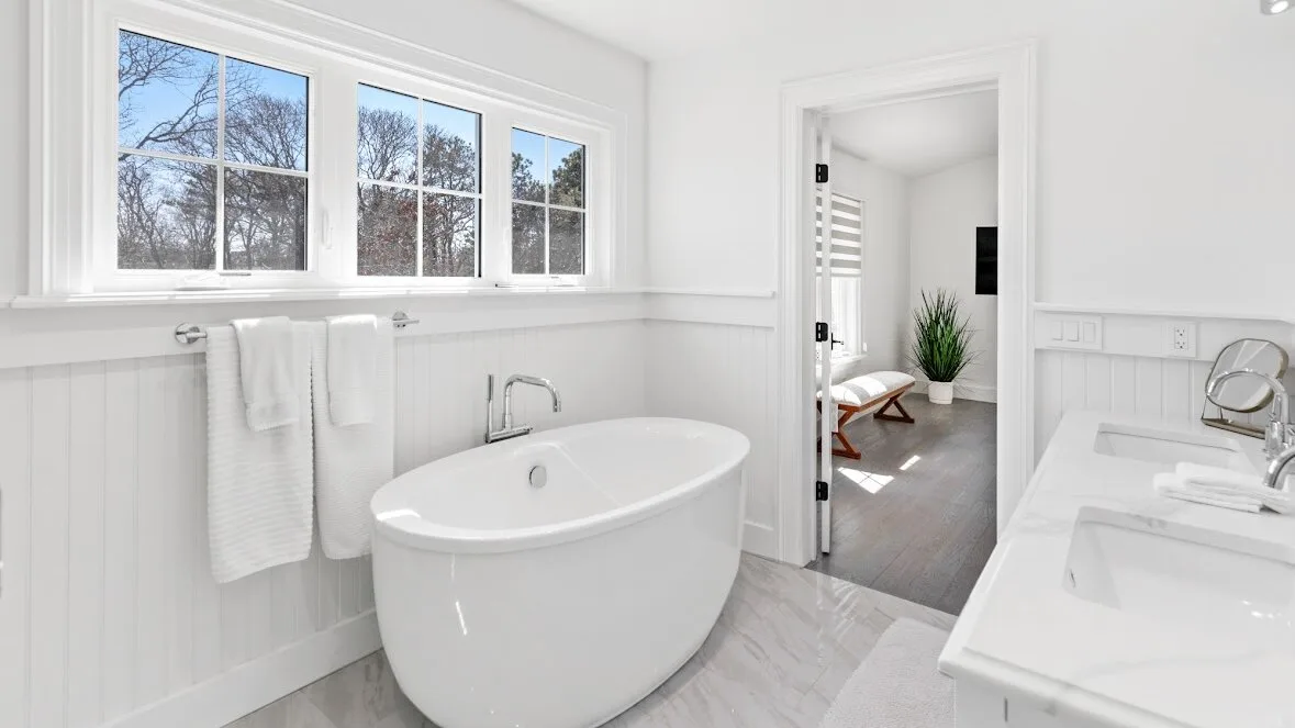 Un baño luminoso con una bañera exenta bajo varias ventanas.