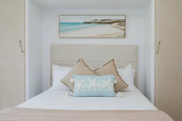 Un dormitorio con una cama tendida y una fotografía enmarcada de una playa sobre el cabecero.