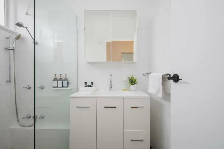 Un baño luminoso con tocador, lavabo y ducha con mampara de vidrio.