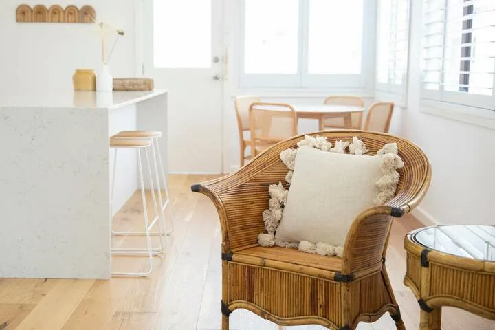 Un comedor luminoso con un sillón de ratán y una mesa junto a las ventanas.