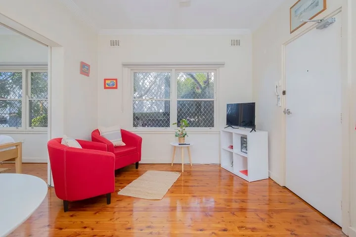 Una sala luminosa con asientos rojos, un televisor y ventanas grandes.