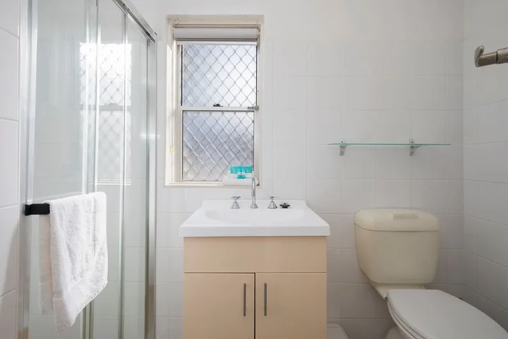 Un baño luminoso con lavabo, inodoro y ducha de vidrio.