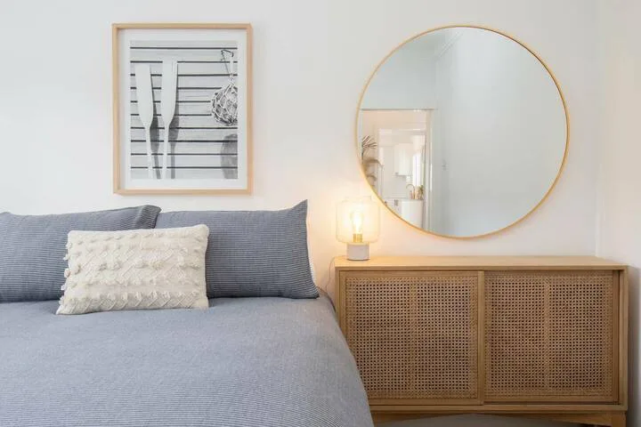 Un dormitorio con una cama junto a un mueble de madera y un espejo redondo.