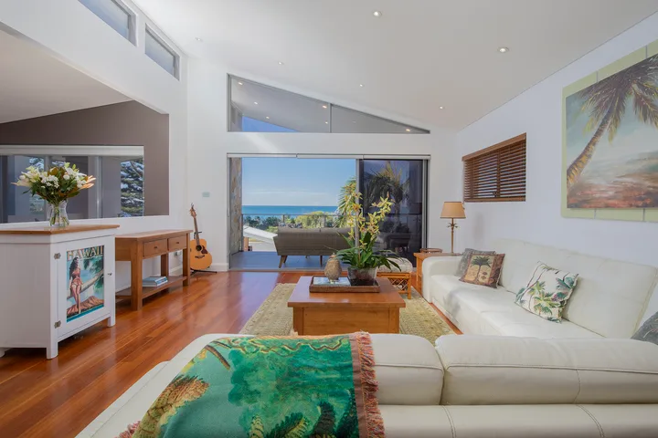 Sala de estar luminosa con asientos blancos y puertas corredizas de vidrio con vista al océano.