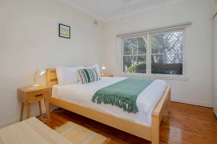 Un dormitorio con una cama de madera, ropa de cama blanca y una manta verde.