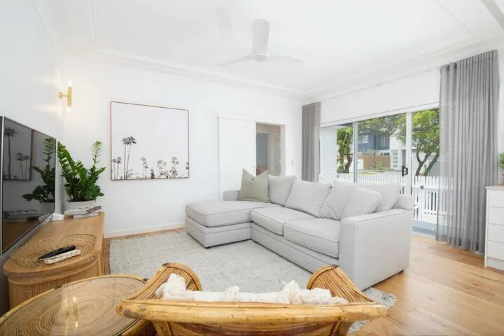 Una sala luminosa con un sofá seccional claro y grandes ventanas.