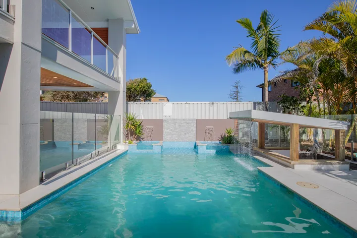 Piscina exterior junto a un edificio moderno, con palmeras al fondo.