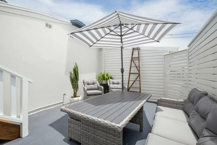 Un patio exterior con asientos acolchados, una mesa y una sombrilla a rayas.